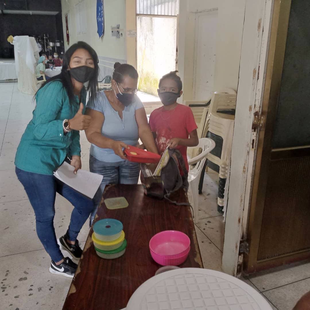Una voluntaria recibe con alegría a una madre y su hija en una jornada de entrega.