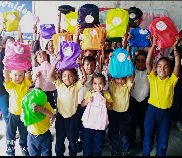 Grupo de niños levanta con alegría los kits escolares de colores que recibieron.