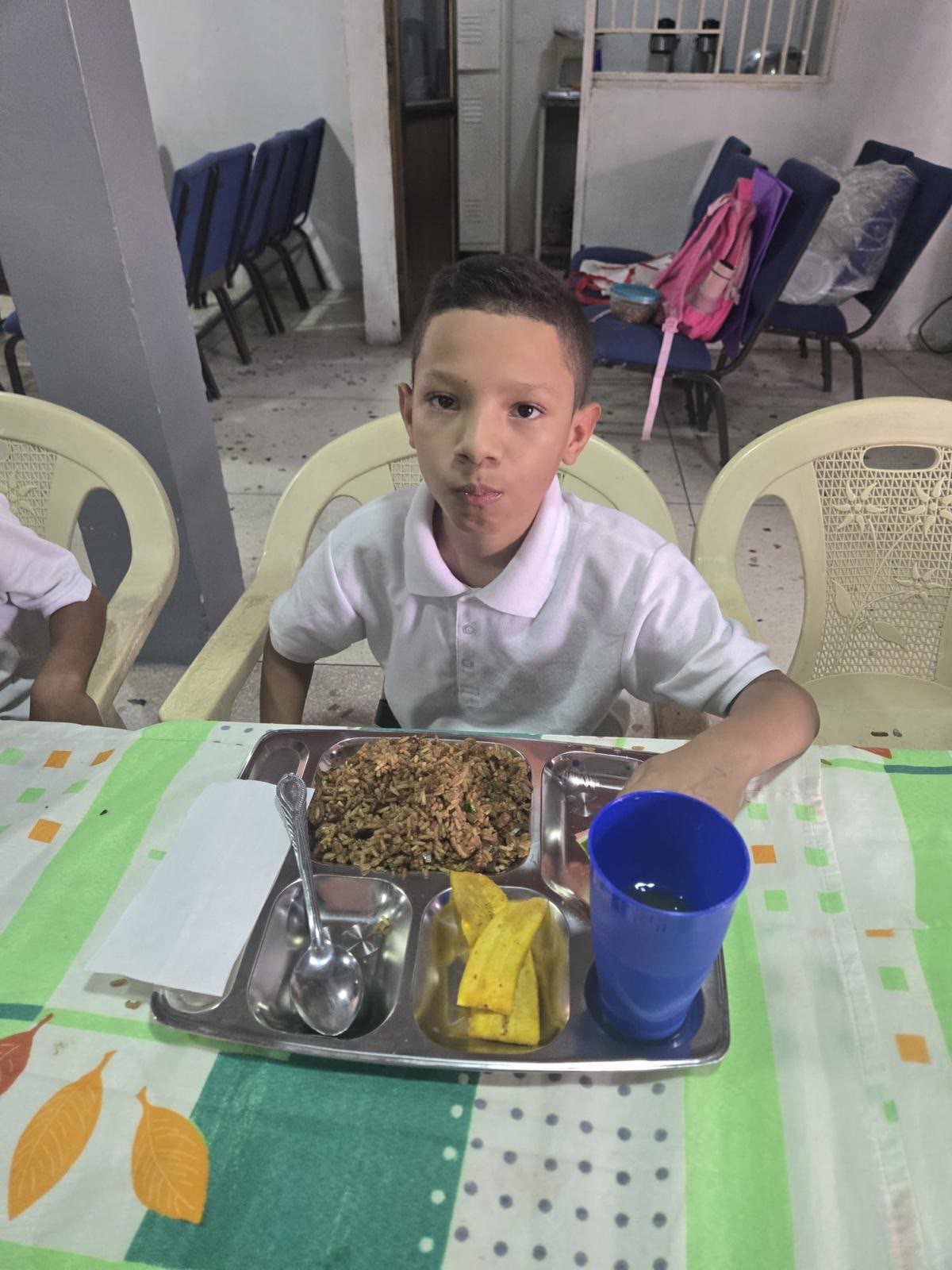 Niño en uniforme escolar disfruta su comida en el comedor comunitario.